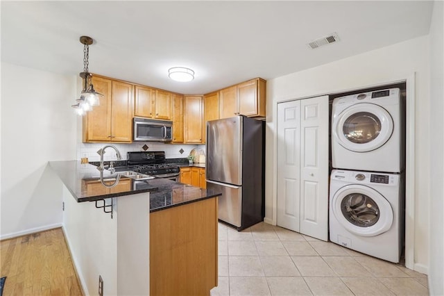 kitchen featuring stacked washer and dryer, visible vents, appliances with stainless steel finishes, dark stone countertops, and a peninsula