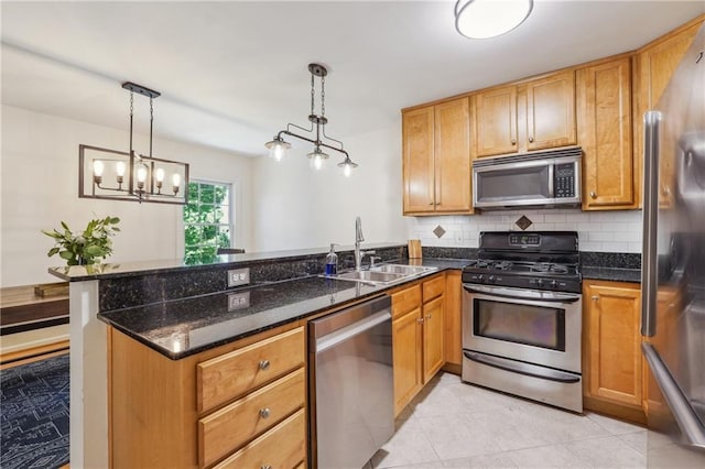 kitchen featuring a peninsula, a sink, appliances with stainless steel finishes, backsplash, and dark stone counters