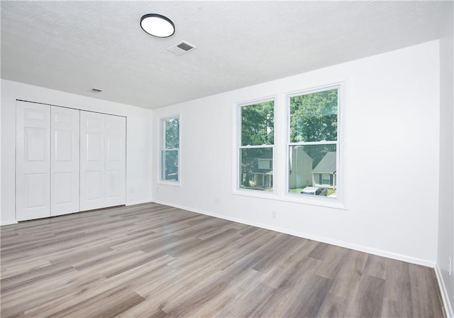 unfurnished bedroom with light wood-type flooring, a textured ceiling, and a closet