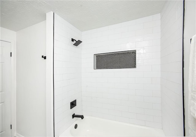 bathroom with a textured ceiling and tiled shower / bath