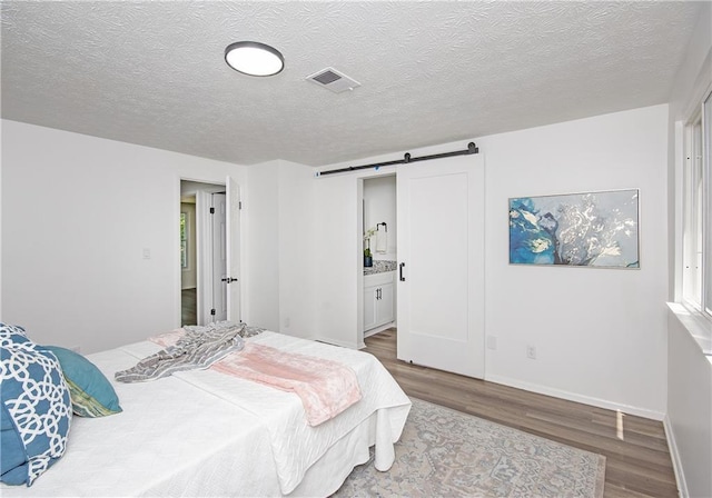 bedroom featuring connected bathroom, a barn door, wood-type flooring, and a textured ceiling