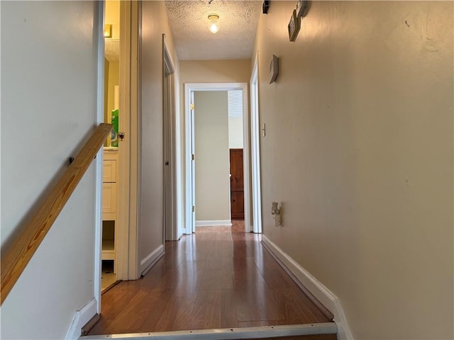 corridor with a textured ceiling, baseboards, and wood finished floors