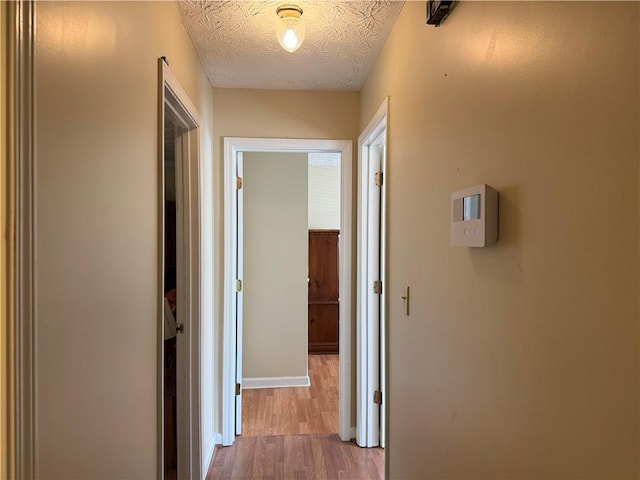 corridor with a textured ceiling, baseboards, and wood finished floors