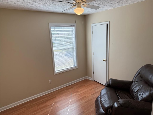 sitting room featuring a ceiling fan, baseboards, light wood-style flooring, and a textured ceiling