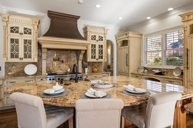 2250 Blackheath Trce, Alpharetta, GA 30005 - kitchen with cream cabinetry, wall chimney exhaust hood, decorative backsplash, a kitchen island with sink, and ornamental molding
