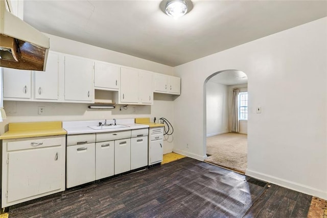 kitchen featuring baseboards, arched walkways, dark wood-type flooring, white cabinetry, and a sink