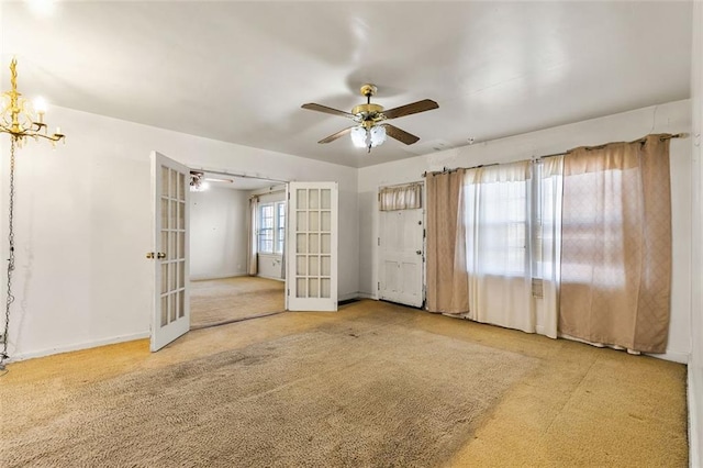 empty room featuring ceiling fan with notable chandelier, carpet floors, french doors, and baseboards