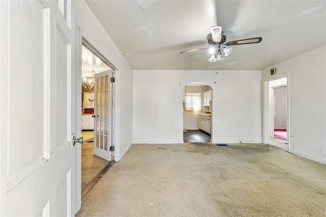 interior space featuring visible vents, arched walkways, baseboards, light colored carpet, and ceiling fan with notable chandelier