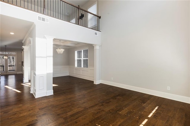 unfurnished living room featuring dark hardwood / wood-style flooring, ornamental molding, decorative columns, and an inviting chandelier