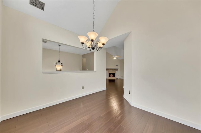 unfurnished dining area with ceiling fan with notable chandelier, hardwood / wood-style floors, and high vaulted ceiling