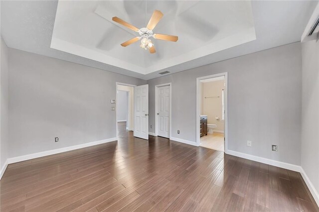 unfurnished bedroom featuring dark hardwood / wood-style floors, a raised ceiling, ceiling fan, and ensuite bathroom