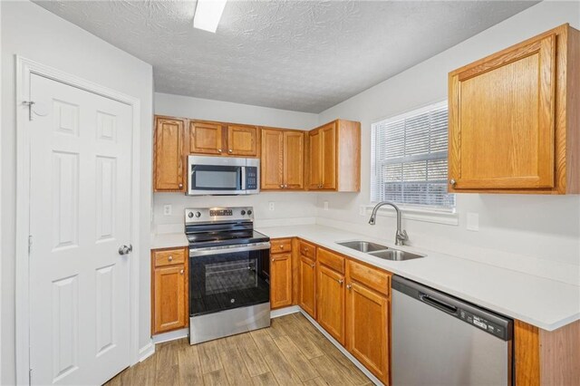 kitchen with sink, stainless steel appliances, a textured ceiling, and light wood-type flooring