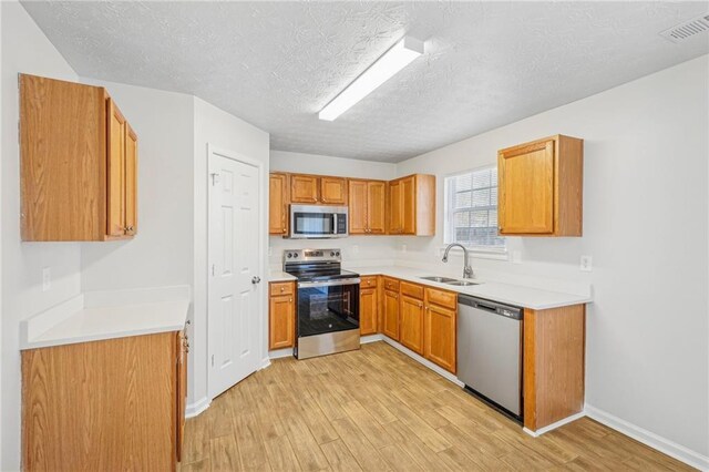 kitchen featuring a textured ceiling, light hardwood / wood-style floors, sink, and stainless steel appliances