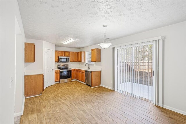 kitchen featuring pendant lighting, sink, a textured ceiling, light hardwood / wood-style floors, and stainless steel appliances