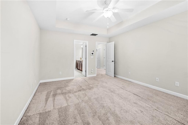 unfurnished bedroom featuring light carpet, a tray ceiling, ceiling fan, and ensuite bathroom