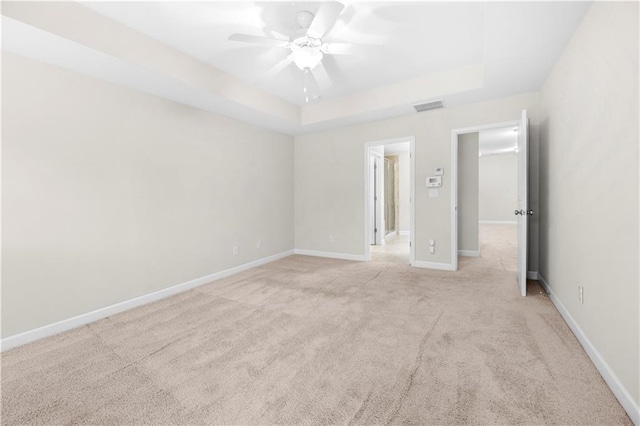 carpeted spare room featuring ceiling fan and a raised ceiling