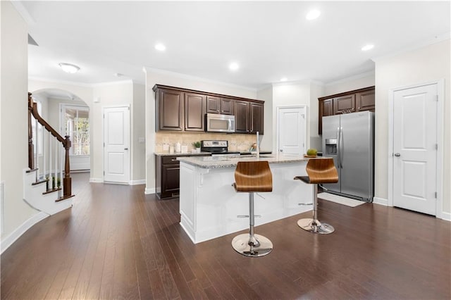 kitchen featuring stainless steel appliances, light stone counters, a breakfast bar area, decorative backsplash, and a center island with sink