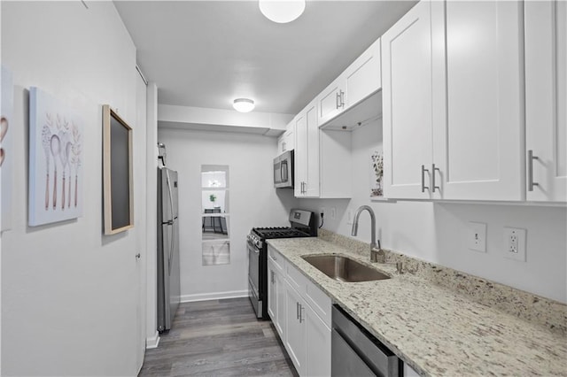 kitchen featuring appliances with stainless steel finishes, a sink, white cabinetry, light stone countertops, and dark wood-style flooring