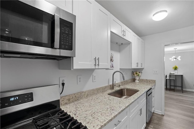 kitchen featuring stainless steel appliances, a sink, light wood-type flooring, white cabinetry, and light stone counters
