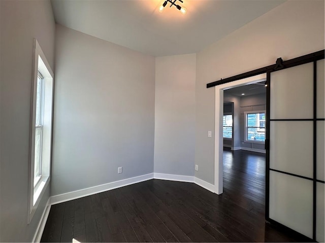 spare room featuring a barn door, baseboards, and dark wood-style flooring