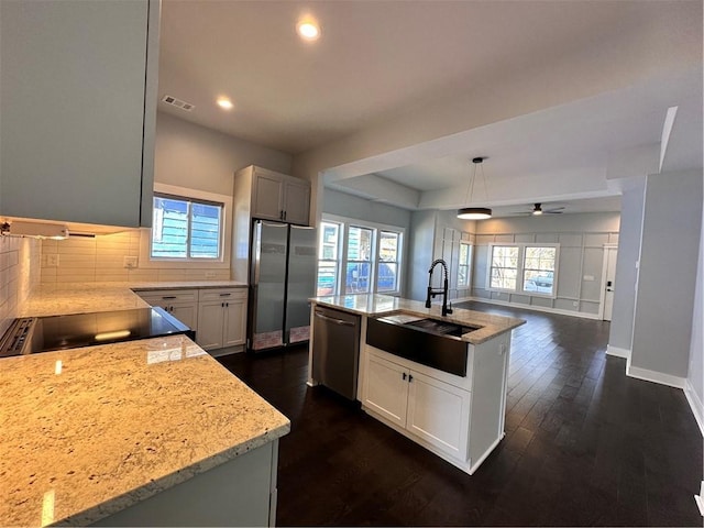 kitchen featuring visible vents, an island with sink, appliances with stainless steel finishes, decorative light fixtures, and a sink