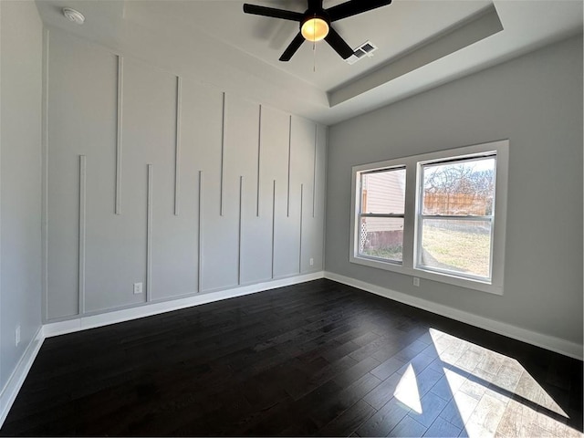 unfurnished bedroom featuring a tray ceiling, dark wood finished floors, visible vents, and baseboards