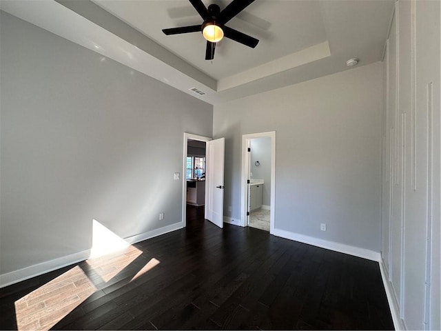 spare room with a ceiling fan, a raised ceiling, dark wood finished floors, and baseboards