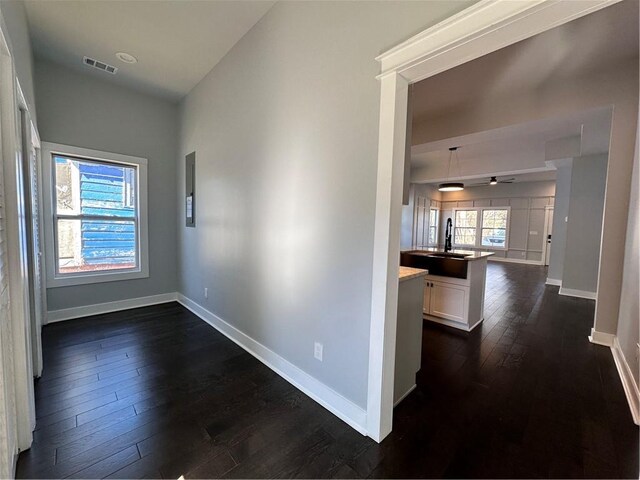 corridor featuring dark wood-style floors, visible vents, a sink, and baseboards