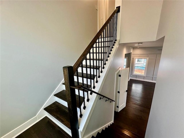 staircase featuring wood finished floors, a towering ceiling, and baseboards