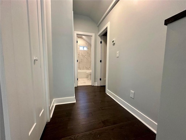 corridor featuring dark wood-style floors, baseboards, and vaulted ceiling