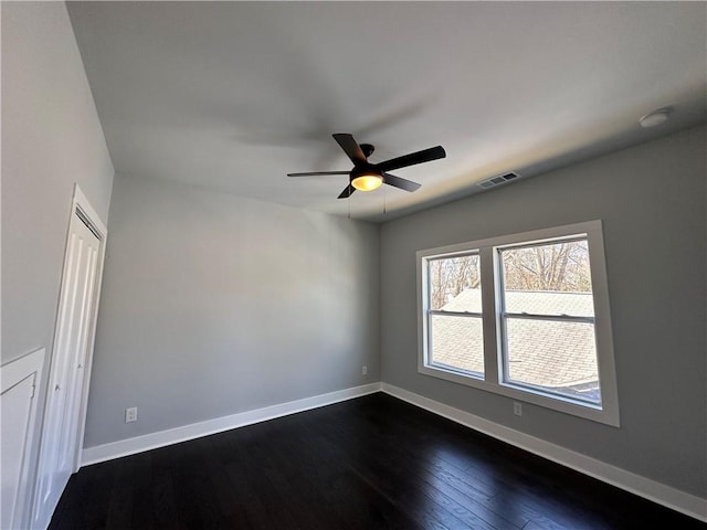 empty room with baseboards, visible vents, ceiling fan, and dark wood-type flooring