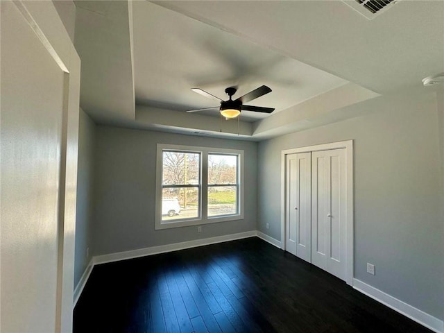 unfurnished bedroom featuring a ceiling fan, baseboards, a raised ceiling, and dark wood finished floors