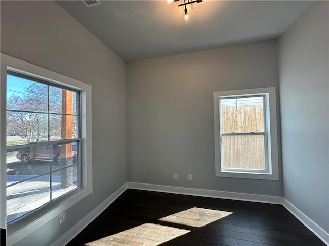 spare room featuring dark wood-style flooring, visible vents, and baseboards