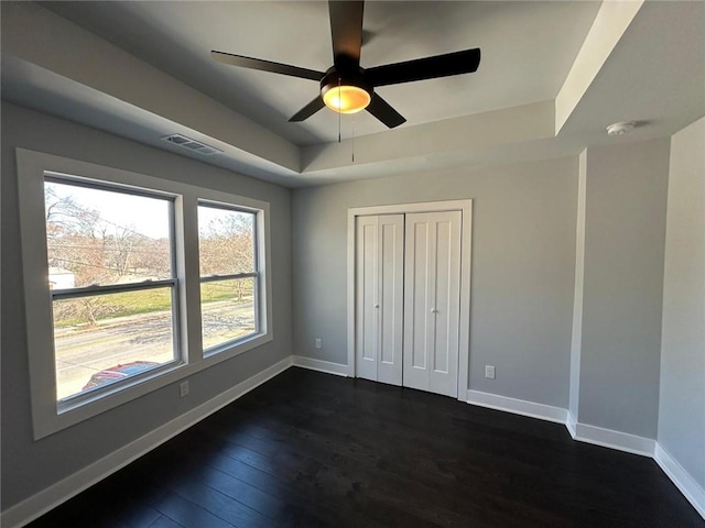 unfurnished bedroom with dark wood-style flooring, a closet, a raised ceiling, visible vents, and baseboards