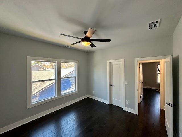 unfurnished bedroom featuring dark wood-style floors, baseboards, visible vents, and ceiling fan