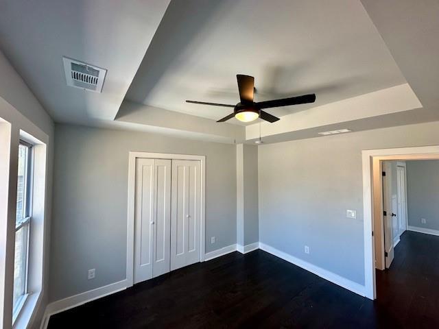 unfurnished bedroom featuring dark wood-style floors, a tray ceiling, visible vents, and baseboards