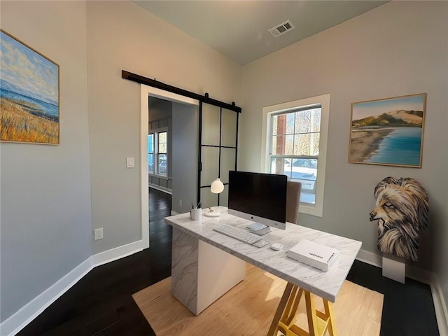 office area featuring a barn door, wood finished floors, visible vents, and baseboards