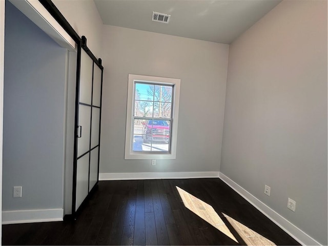 empty room featuring visible vents, dark wood finished floors, baseboards, and a barn door