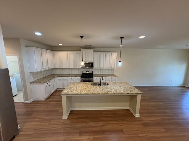 kitchen with an island with sink, a sink, appliances with stainless steel finishes, decorative backsplash, and dark wood-style flooring