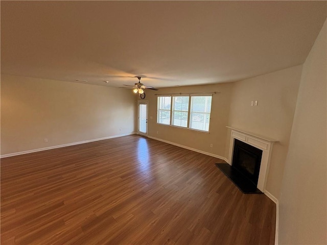 unfurnished living room featuring a ceiling fan, dark wood-type flooring, a fireplace with raised hearth, and baseboards