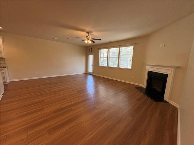 unfurnished living room with a fireplace with raised hearth, a ceiling fan, baseboards, and dark wood-style flooring