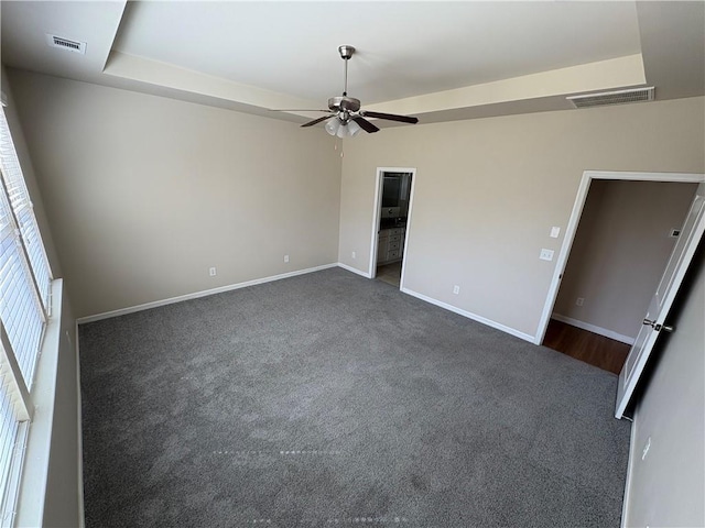 empty room with dark colored carpet, visible vents, baseboards, and ceiling fan