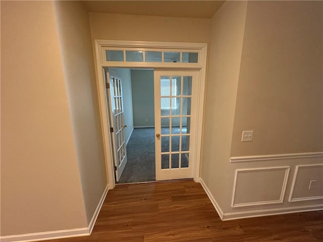 hallway with dark wood-type flooring, baseboards, wainscoting, french doors, and a decorative wall