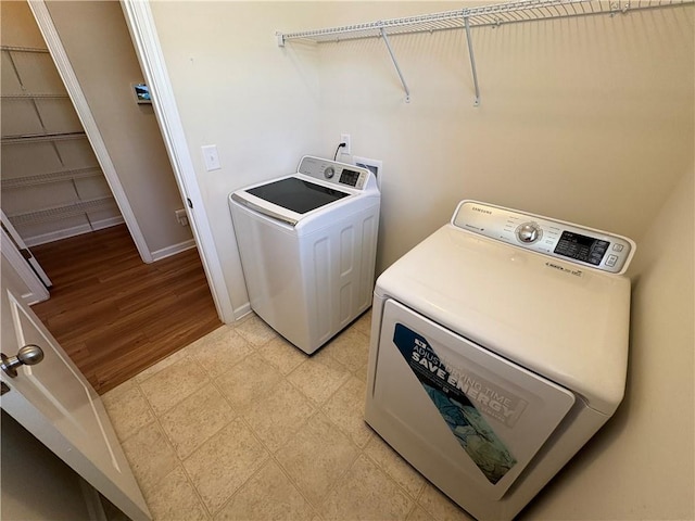 washroom featuring laundry area, washing machine and dryer, baseboards, and light floors