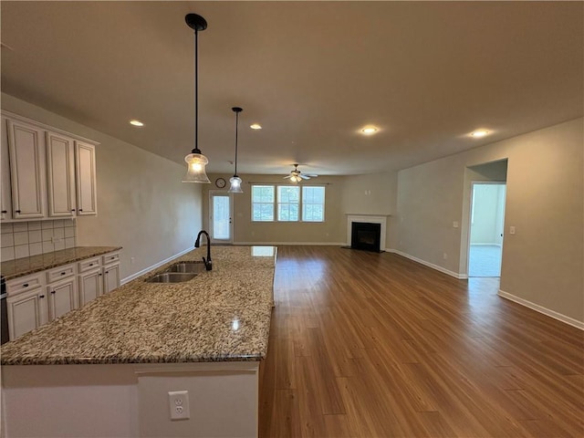 kitchen featuring a fireplace with flush hearth, a sink, wood finished floors, decorative backsplash, and ceiling fan