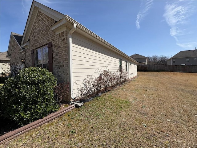 view of home's exterior with a yard, brick siding, and fence