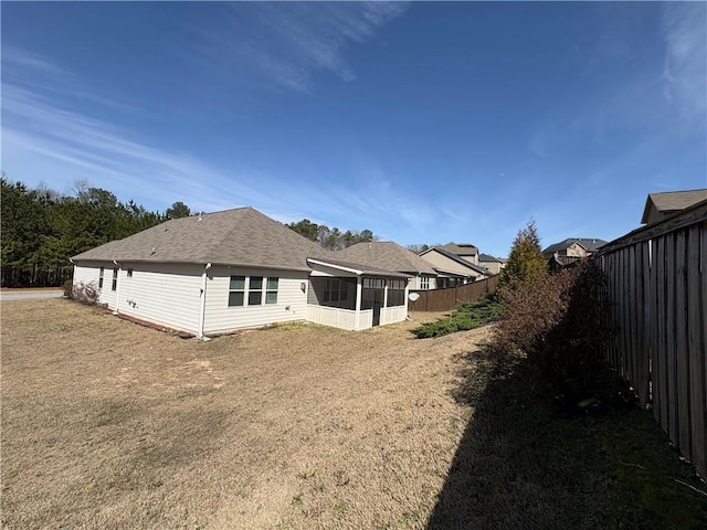 rear view of house featuring a yard, a fenced backyard, and a sunroom