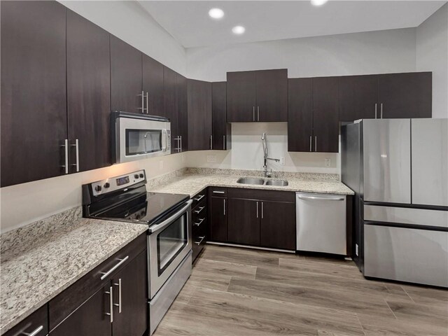 kitchen featuring light wood-type flooring, appliances with stainless steel finishes, light stone countertops, sink, and dark brown cabinets