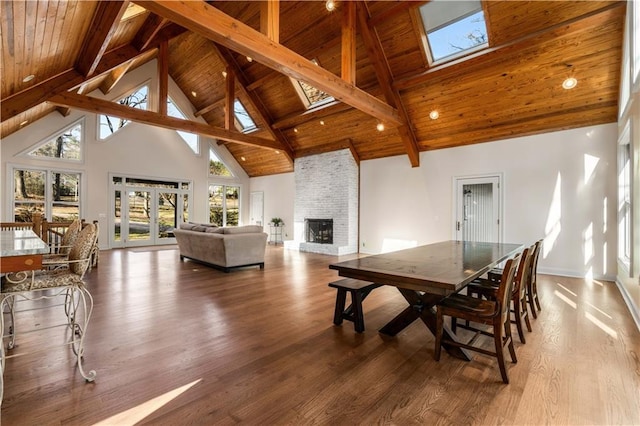 dining room with wood-type flooring, a skylight, wooden ceiling, a large fireplace, and beamed ceiling