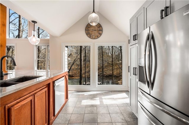 kitchen with pendant lighting, sink, dishwashing machine, stainless steel fridge, and light stone counters